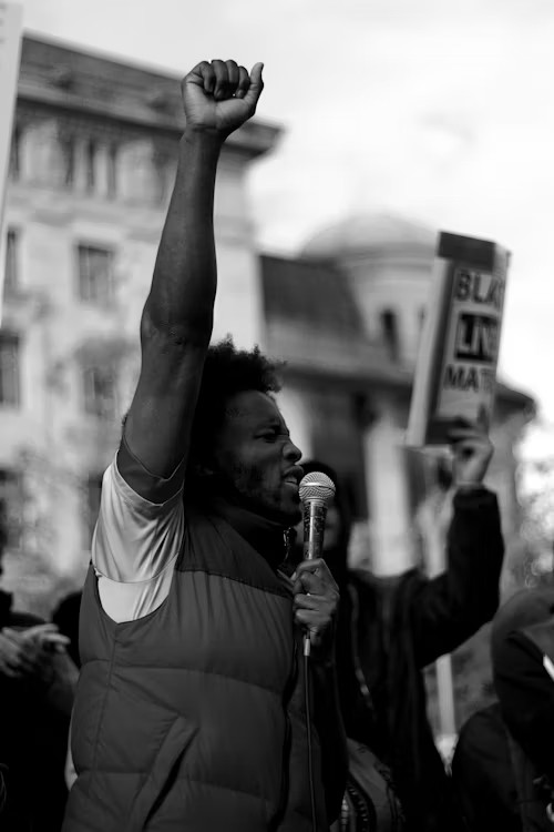 Orateur avec micro, poing levé — mobilisation et solidarité pour les droits et la justice sociale.